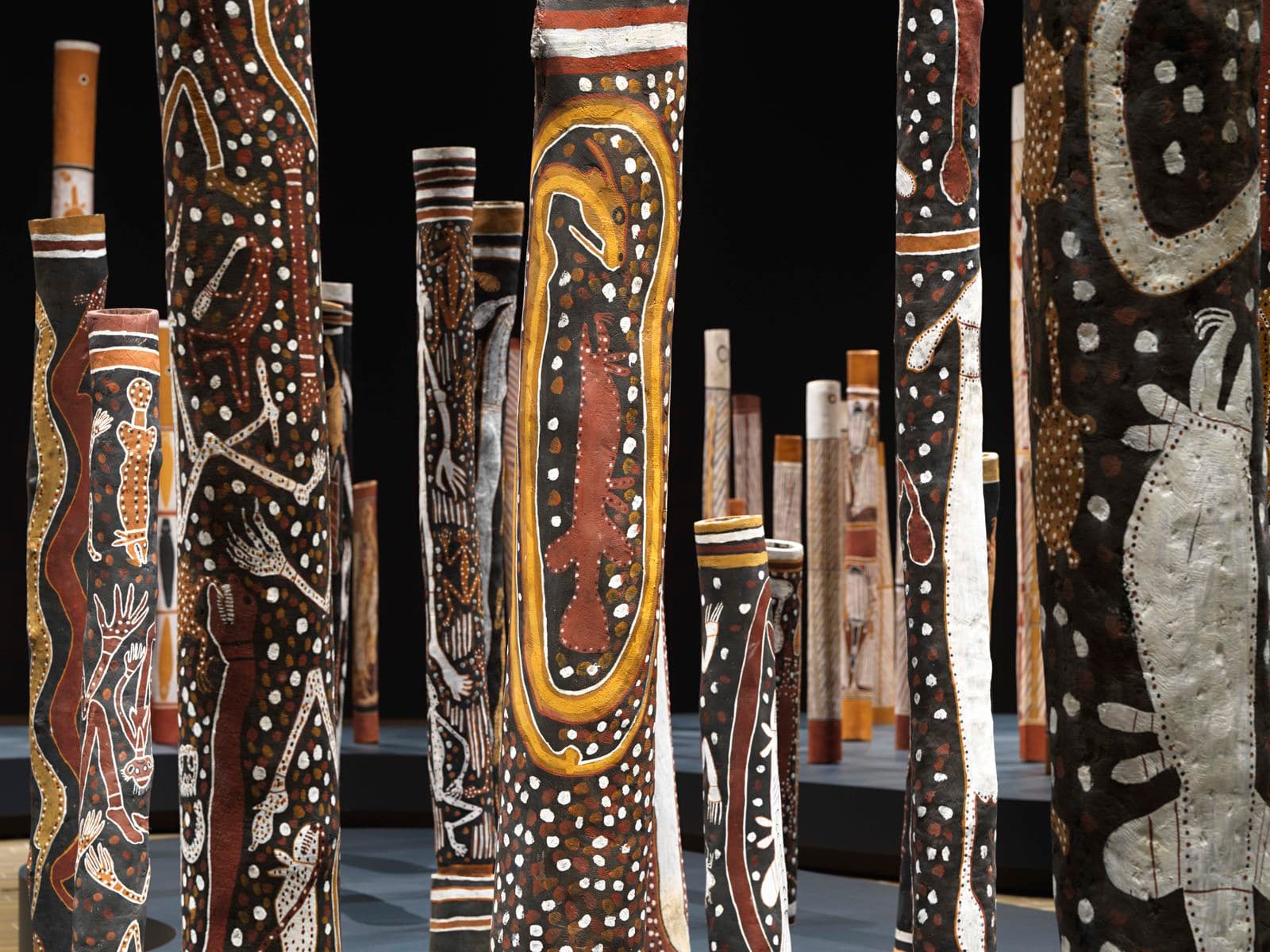 First Nations work of art detail of painted black hollow logs on display in dark exhibition space