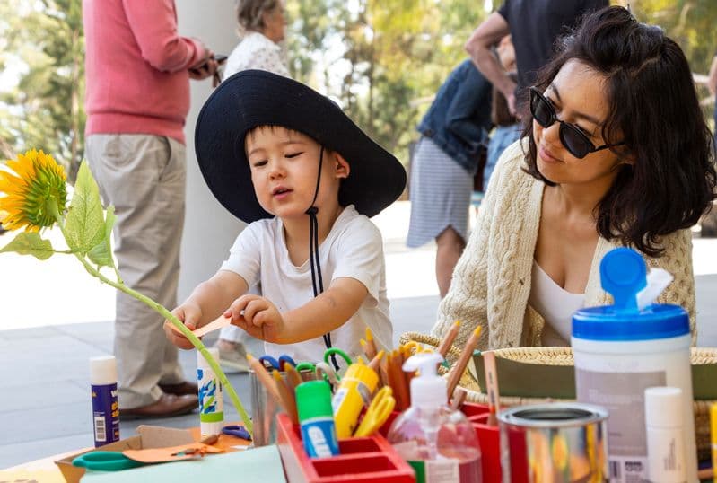 A young boy and his mother sit at a table of artmaking materials doing an activity