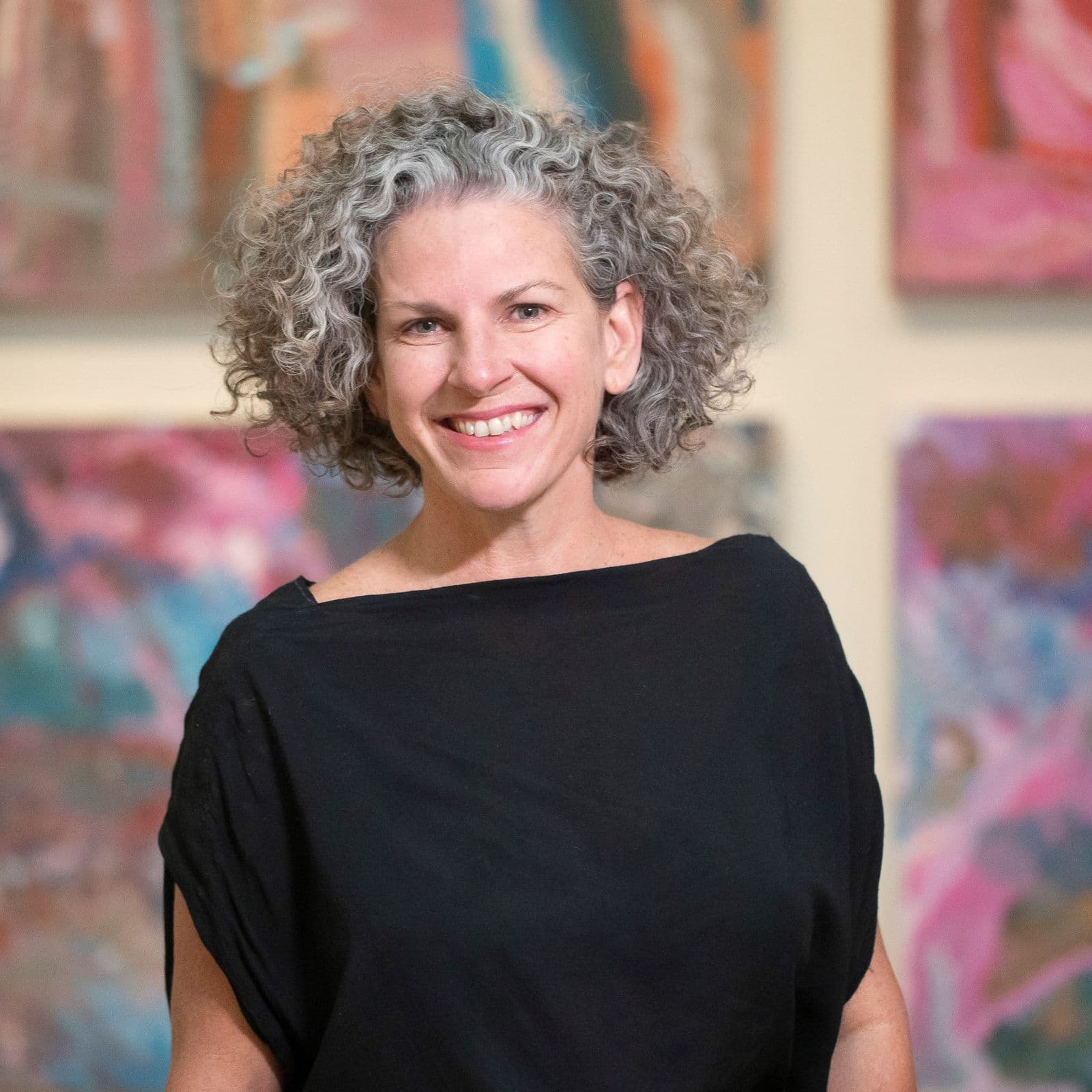 A close up of a woman standing in front of colourful works of art