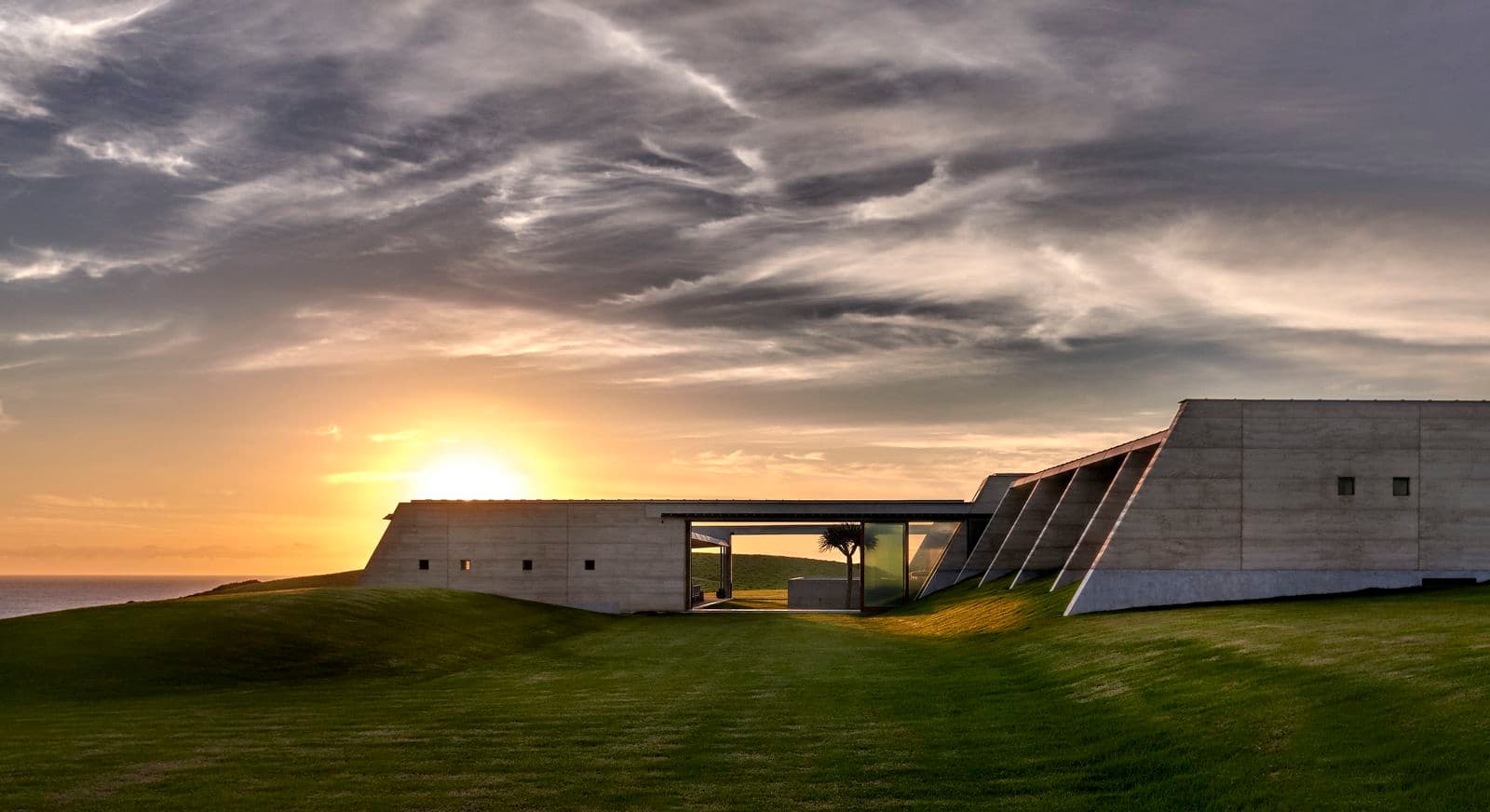 Photograph of grey building on grass at sunset