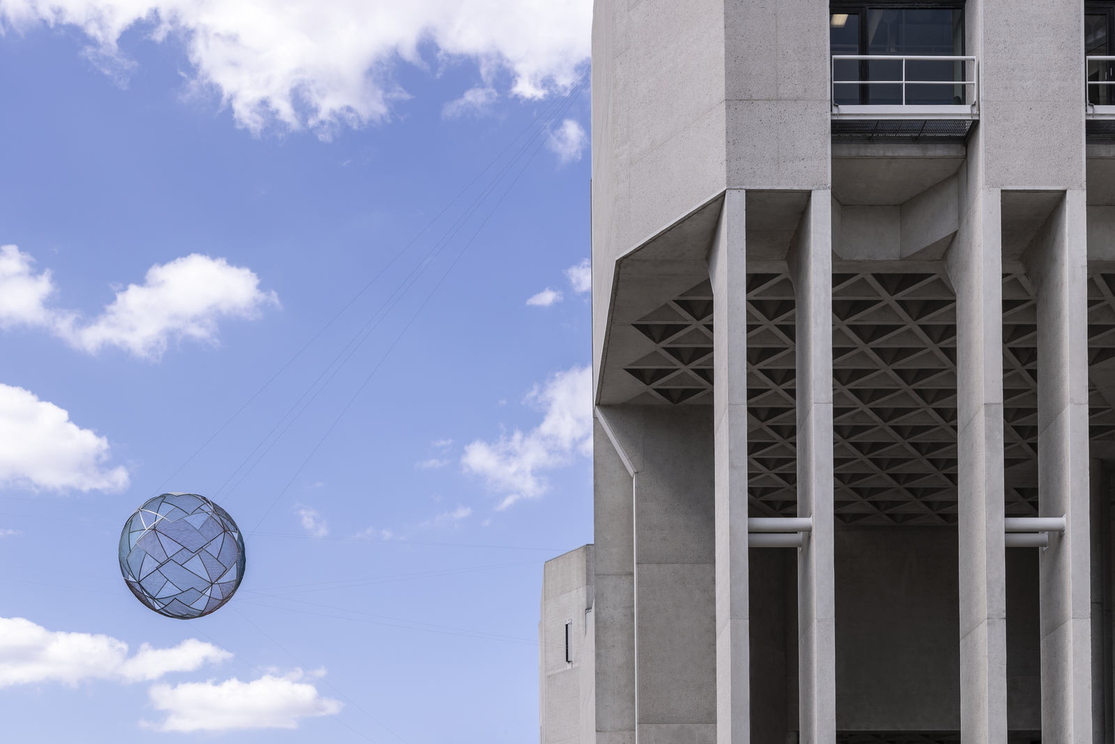 Photograph of building exterior with blue sky and wire sphere sculpture