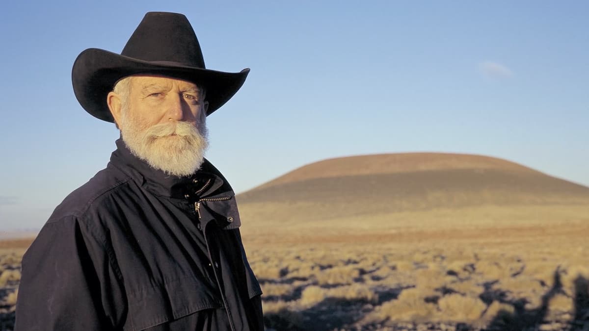 A video still of a man looking ahead in front of a landscape
