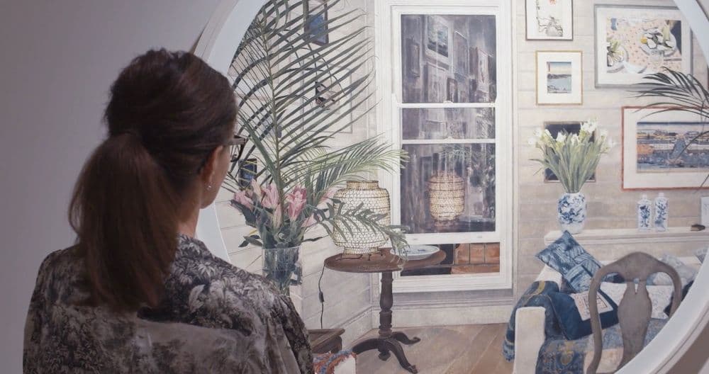 Video of still of the back of a woman wearing a floral pattern shirt with hair in ponytail, looking at a work of art in a gallery of an home interior scene