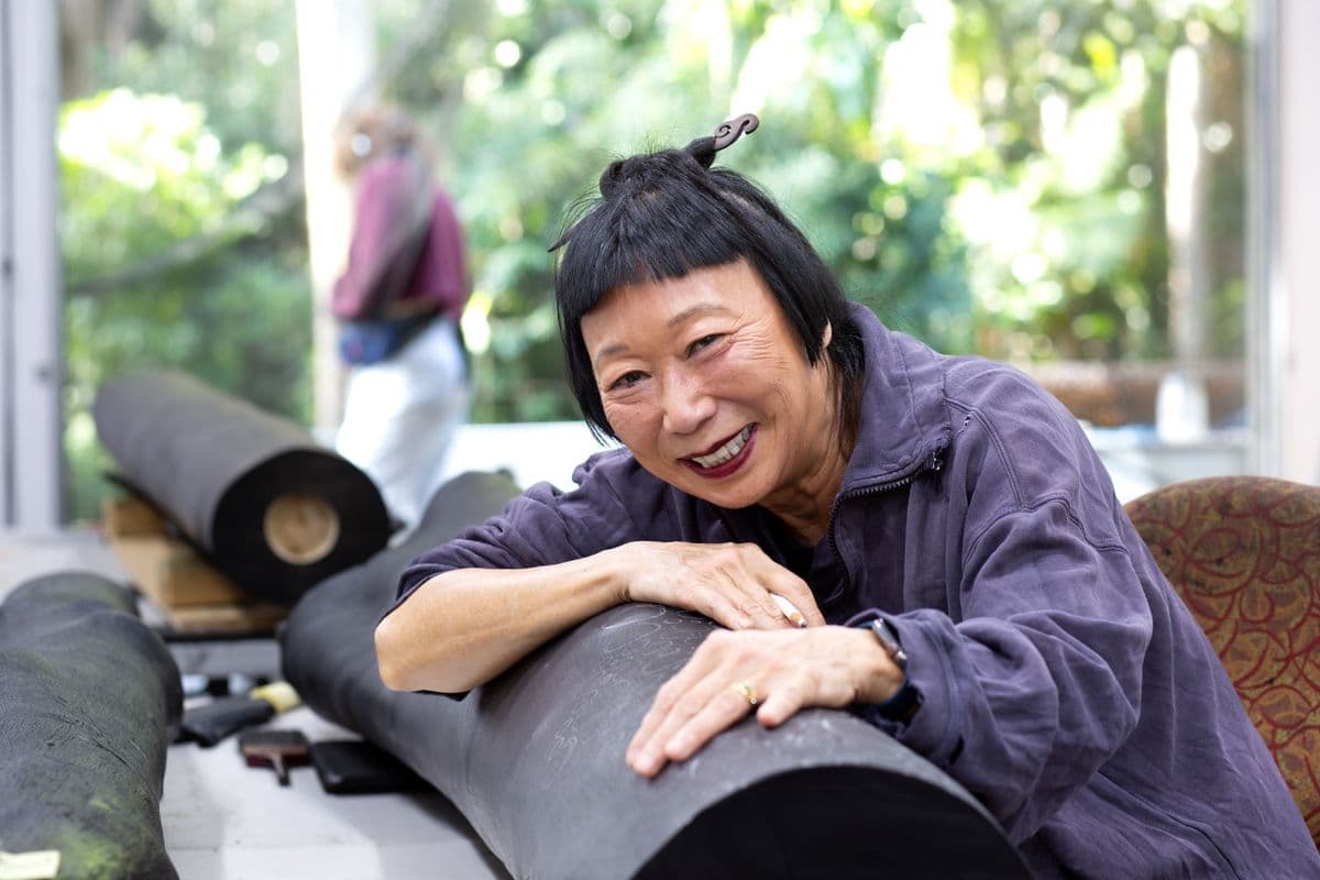 A woman sits drapped over a large round object in a busy studio.