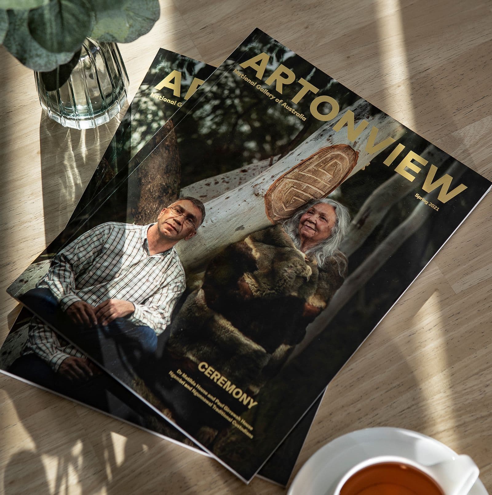 Two Artonview magazines stacked on top of each other on a wooden table next to a glass vase