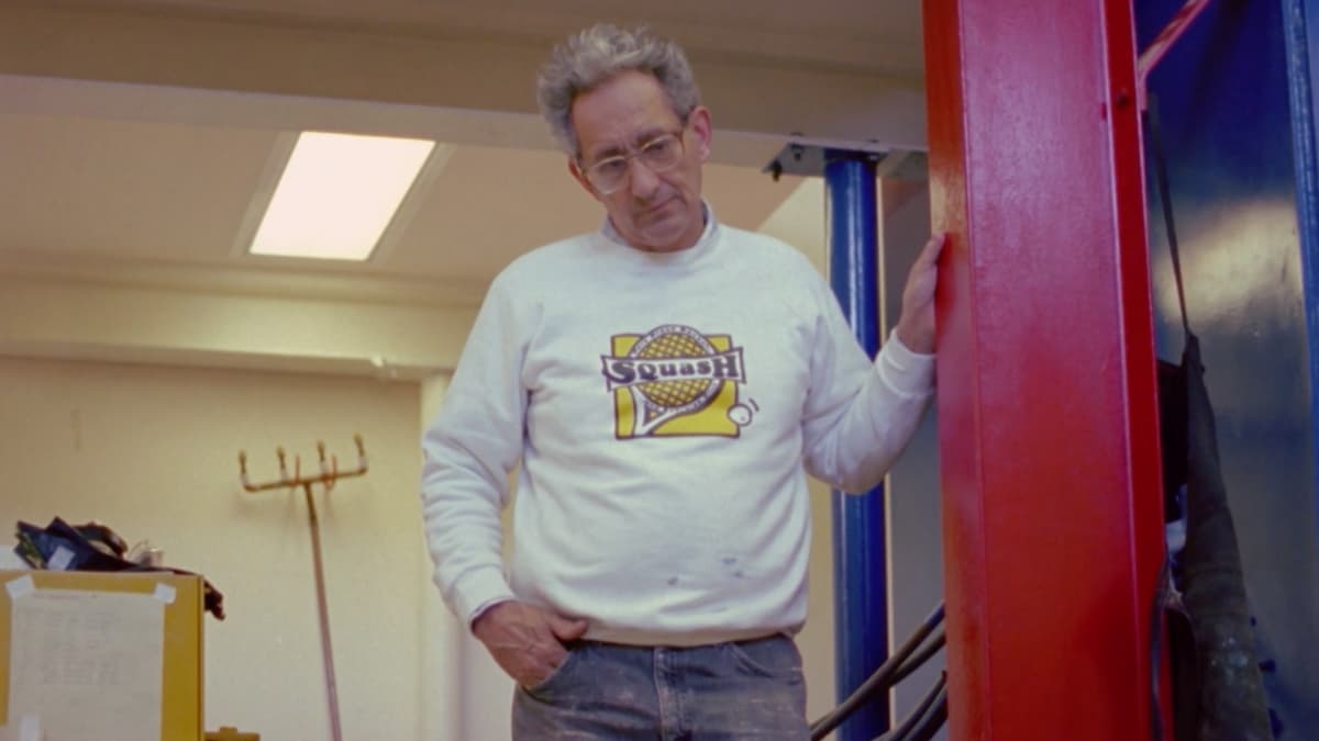 A video still of a man overlooking work in a studio