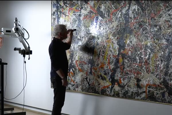 screen capture of a video where a conservator is looking at a large painting of a man using a UV light to examine the canvas