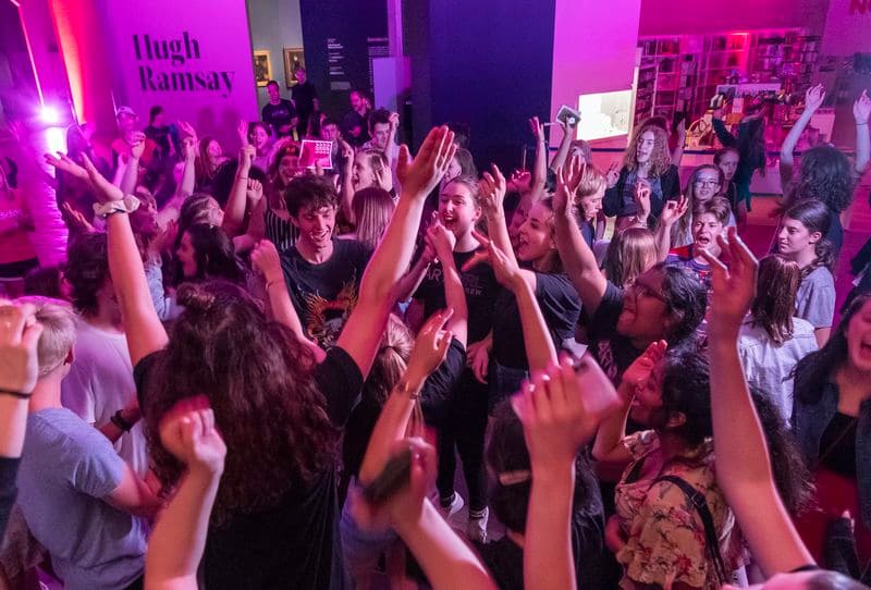 a group of young people are dancing with their arms up in the air under coloured purple lighting