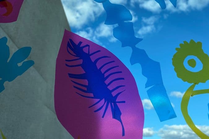Colourful stickers of various shapes stuck on a window with blue sky and clouds seen in background