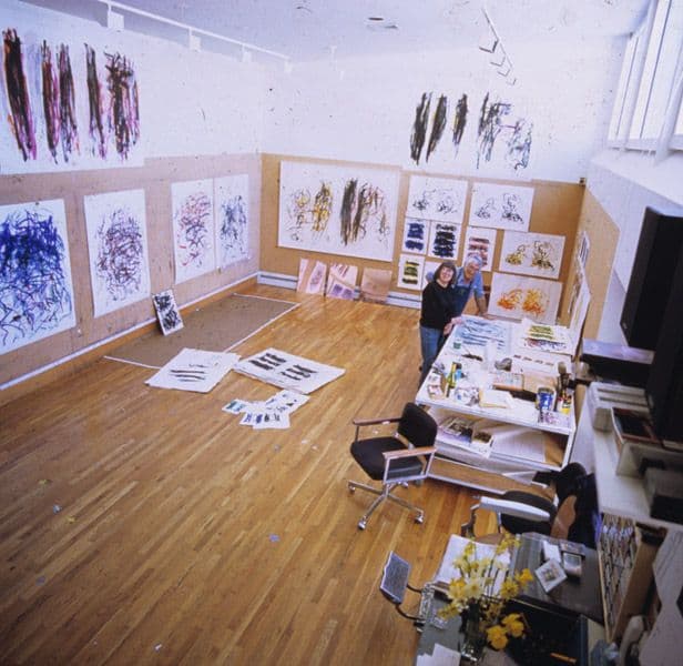 Joan Mitchell and Kenneth Tyler surrounded by numerous prints by Mitchell on the walls, floors and table.