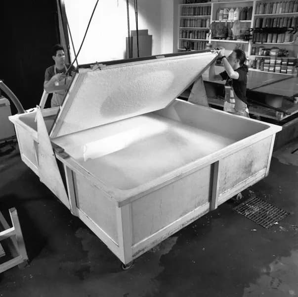 Black and white image of two men using machinery to move the paper pulp sheet