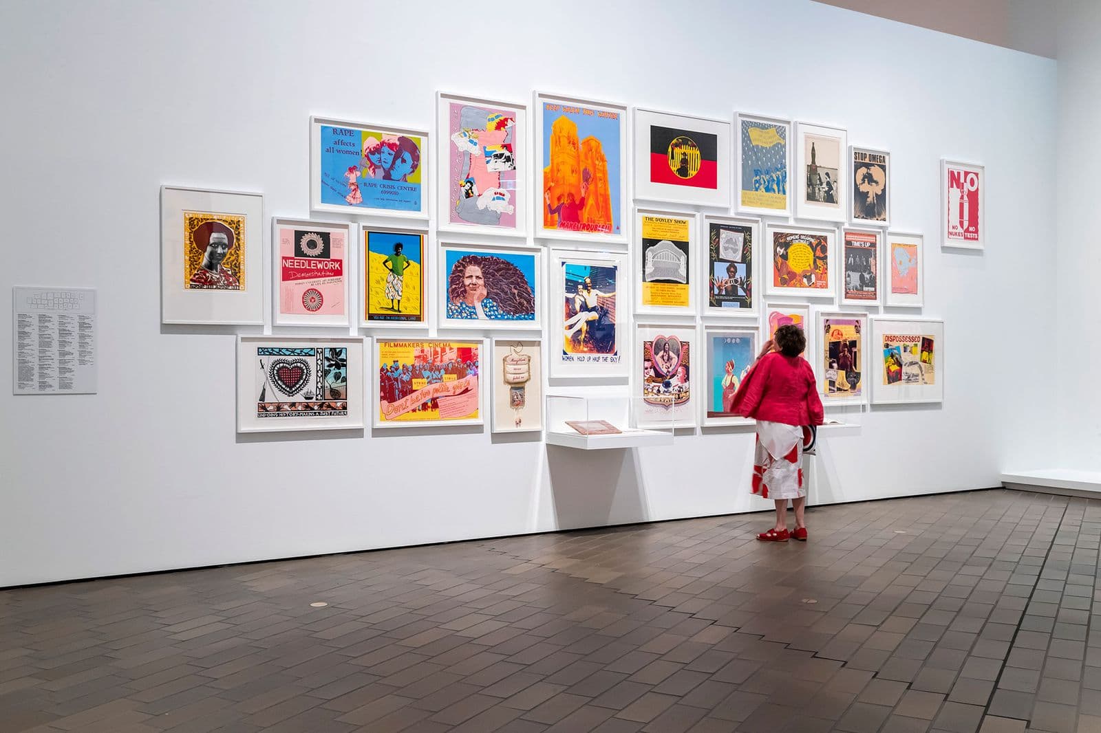 In a large galley space a woman examines a wall of framed and bright posters