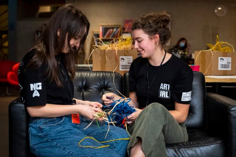 Two teenage girls sitting on a couch, crafting with strips of colourful paper