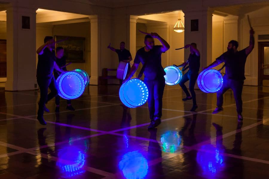 A group of people playing neon drums in a darkly lit room