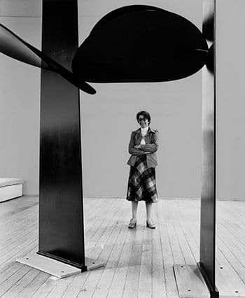 Black and white photograph of female artist in front of large metal sculpture