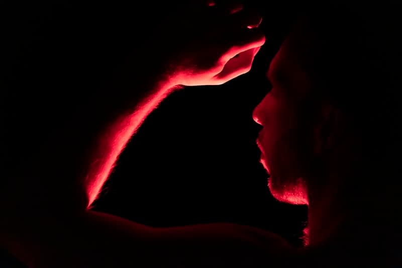 A close up image of Joel Bray dancing with red lighting behind him