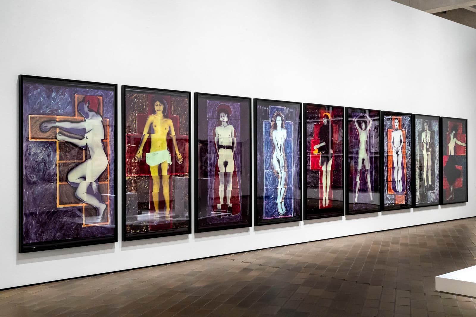 A landscape image of a series of nine large works of art hanging on a gallery wall