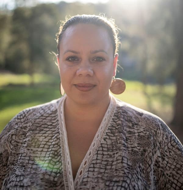 Portrait photo of a female standing outside wearing a patterned blouse, hair pulled back and wearing round earrings