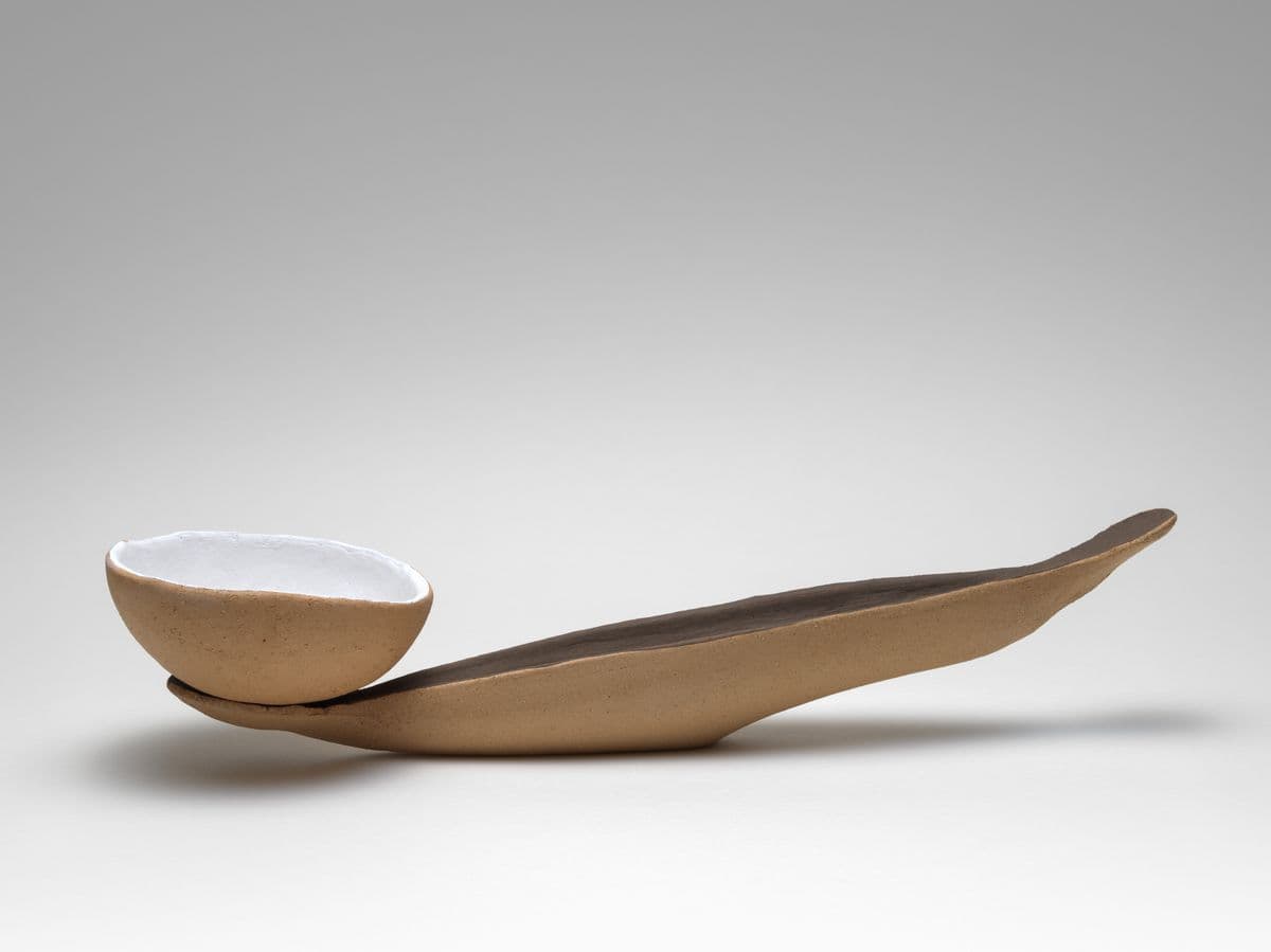 Abstract sculpture of a coconut like bowl weighing down a diagonal ceramic vessel