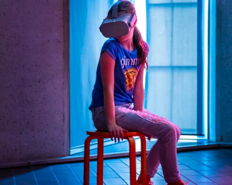Photograph of young person sitting on stool wearing virtual reality headset