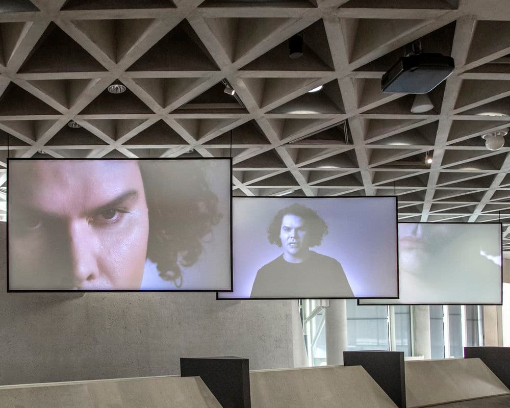 Three large screens hang from the ceiling in a photograph of the Gallery spaces.