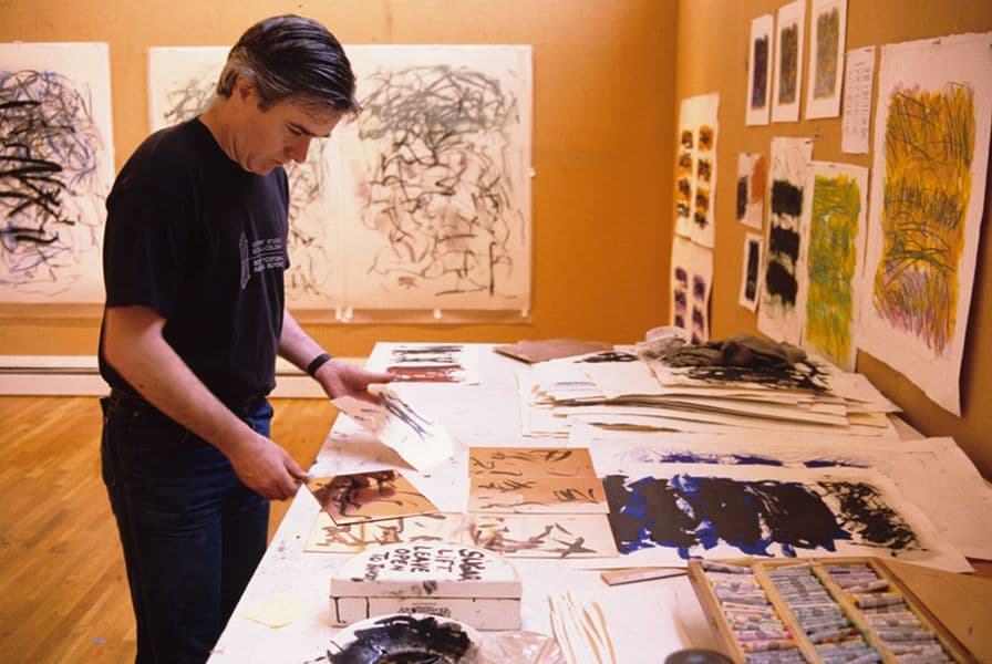 Colour photograph of Anthony Kirk arranging Joan Mitchell proofs on table with numerous Mitchell proofs on walls