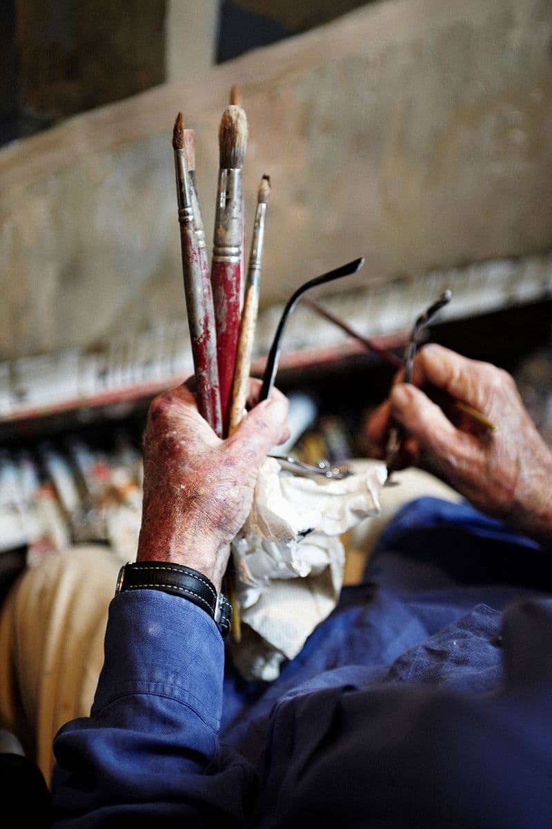 A photograph of a hand holding paintbrushes