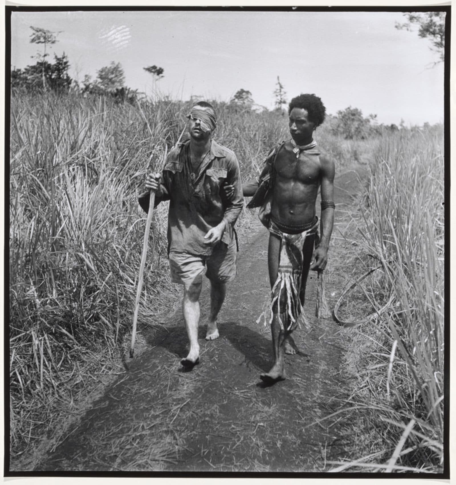 Black and white photograph of Pte George Whittington being led to an aid station by Raphael Oimbari