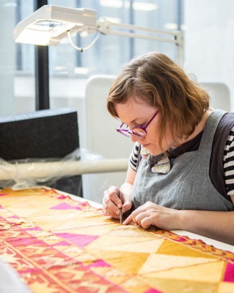 Close up photograph of conservator fixing colourful textile on table