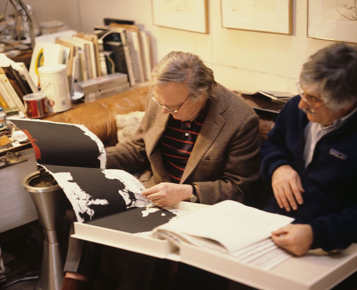 Two men looking through pages of a large book of art