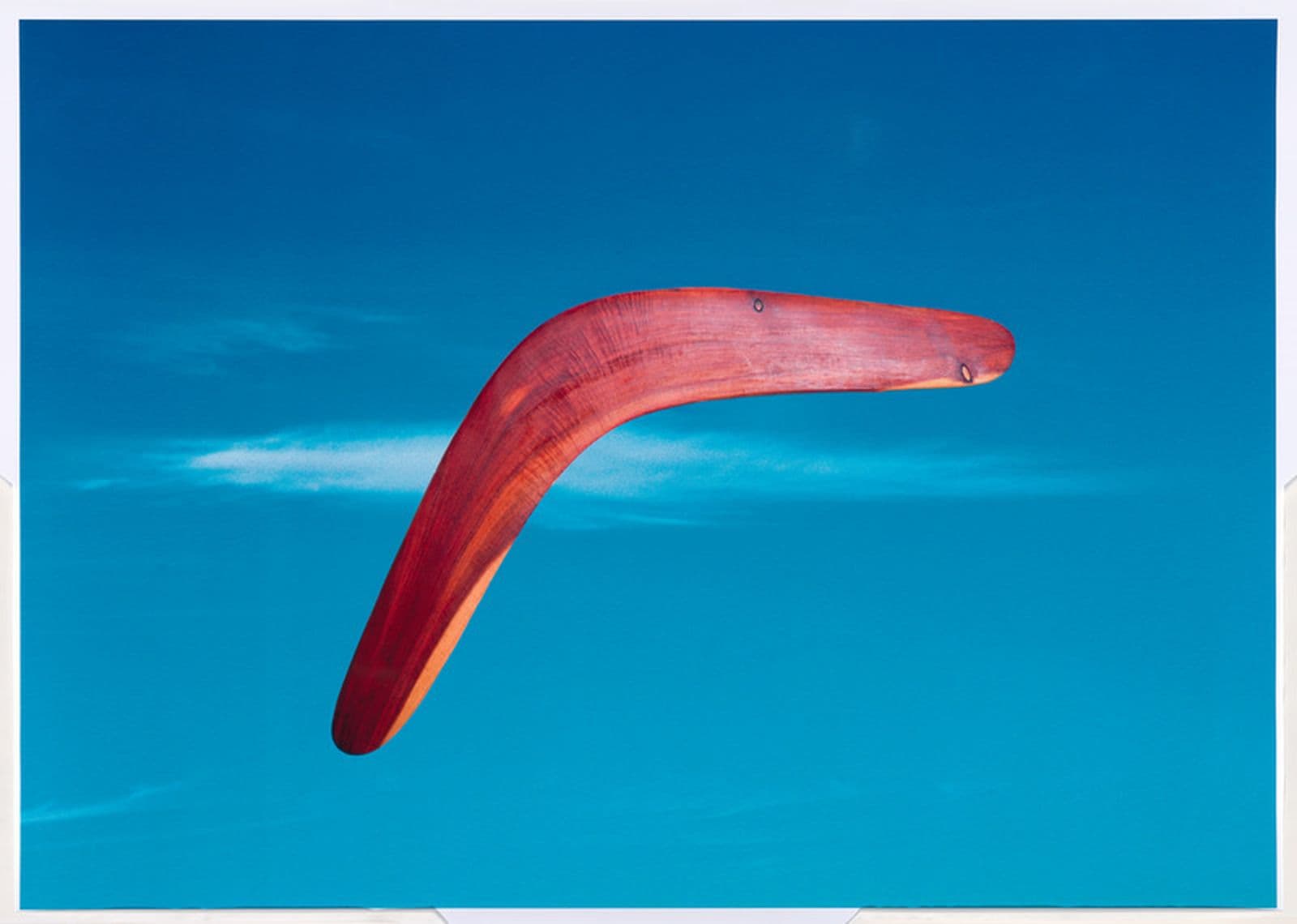 A red timbre boomerang is flying through a bright blue sky