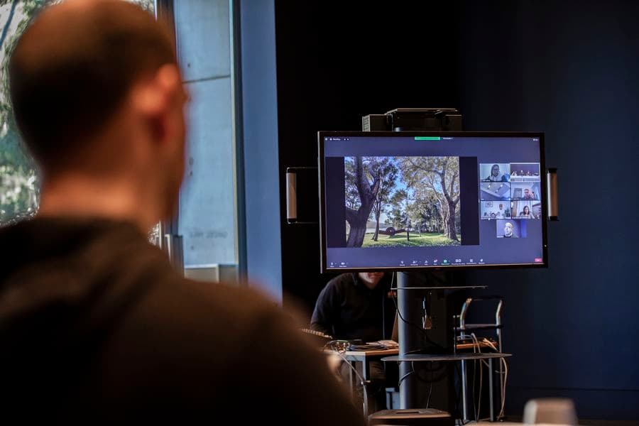 In a large hall a man is looking at a large screen displaying a presentation via conference call.