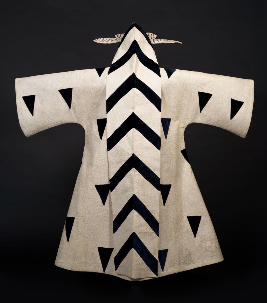 A white robe and headdress with black upside down v shapes in a line on the headress and black triangles on the sleeves and body of the robe