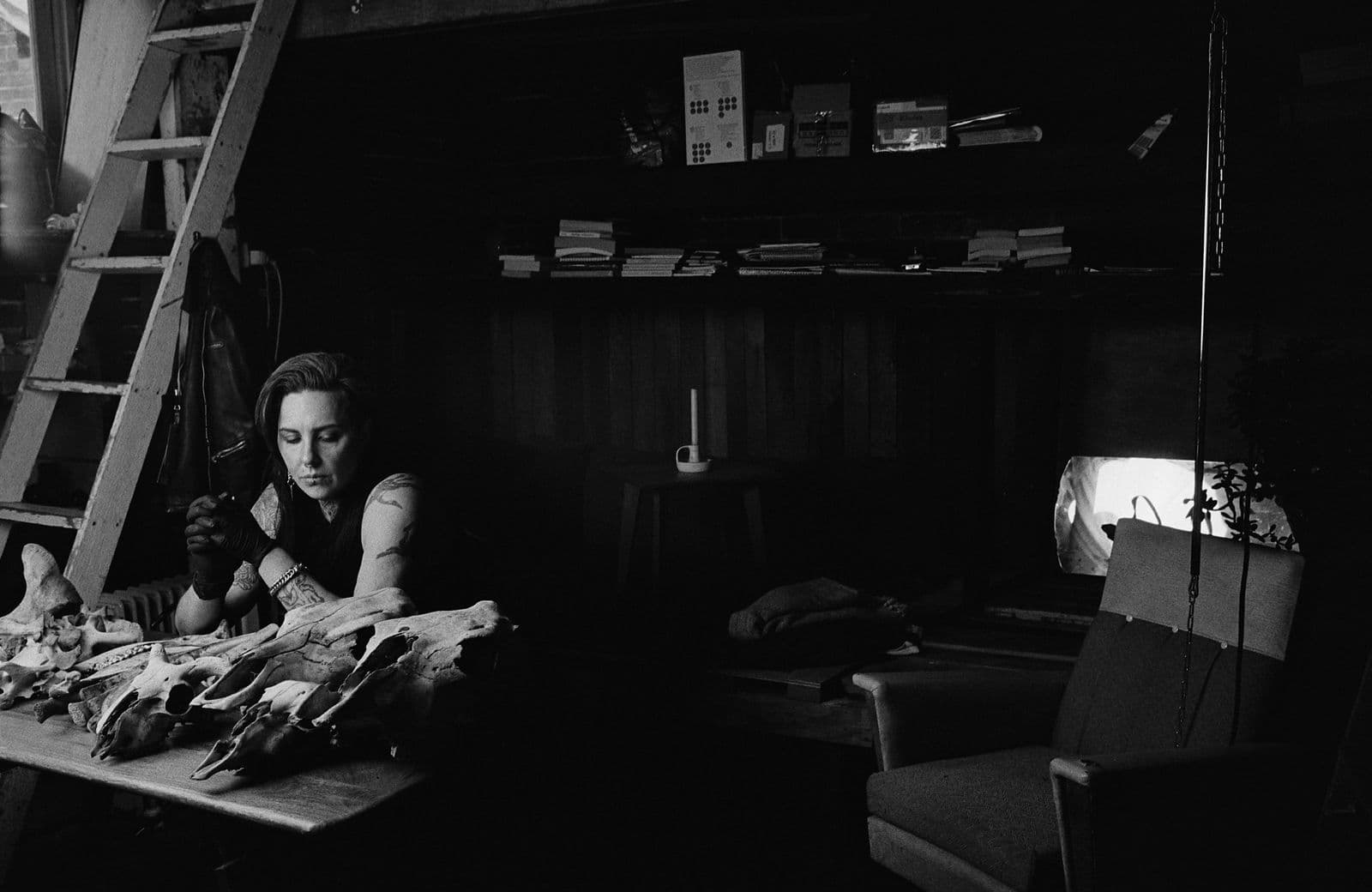 Black and white photograph of Koori artist SJ Norman sitting at a table surrounded by animal bones