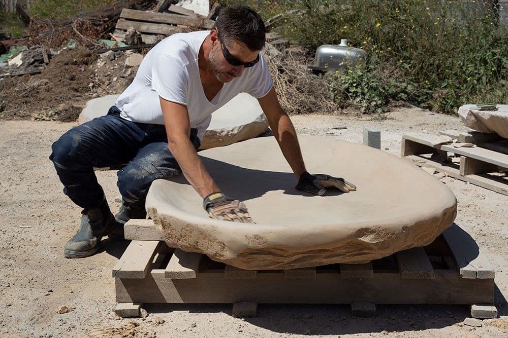 A photograph of the artist sitting and working on a sculpture