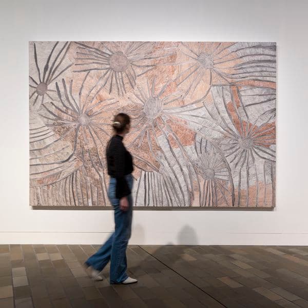 Woman in dark clothing walking in front of art in gallery space