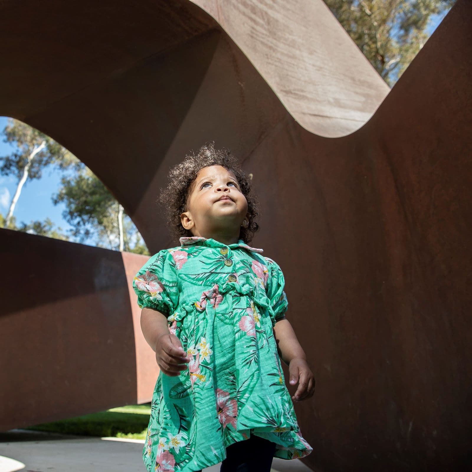 A toddler stands inside a large metal twisting sculpture