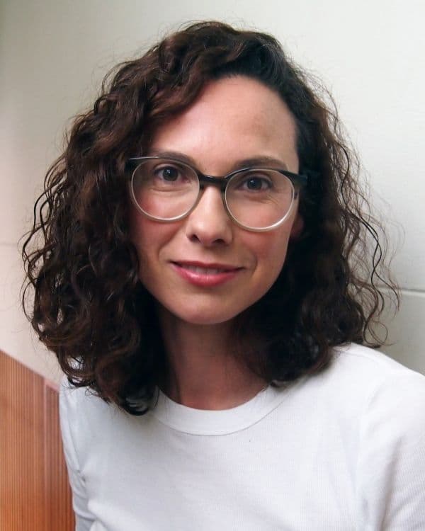 Portrait of young female with dark wavy shoulder length hair wearing glasses and a white t-shirt