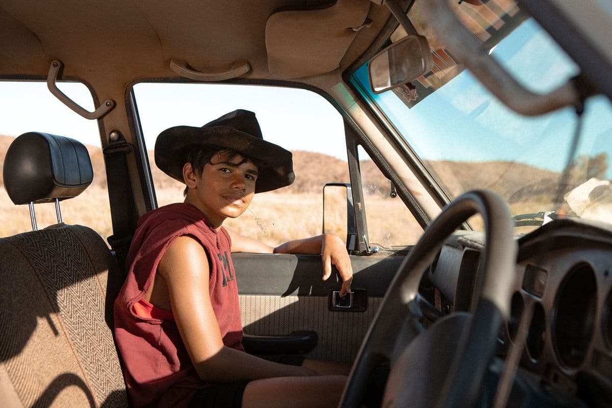 A kid wearing a hat sits on the passenger side of a truck