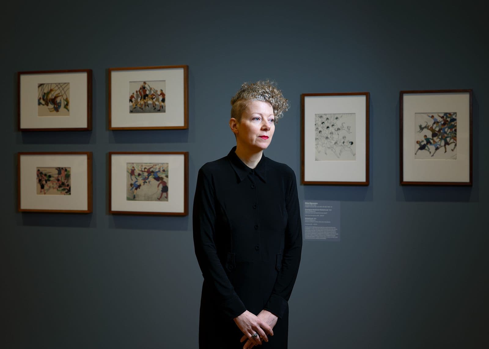 Curator Dr Sarina Noordhuis-Fairfax stands in the Know My Name: Making it Modern exhibition at the National Gallery of Australia surrounded by the work of Ethel Spowers and Eveline Syme