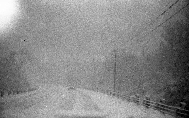A flurry of beautiful snow blankets a road like icing sugar atop a christmas cake. Visibility reduces, creating a hazardous driving scenario.