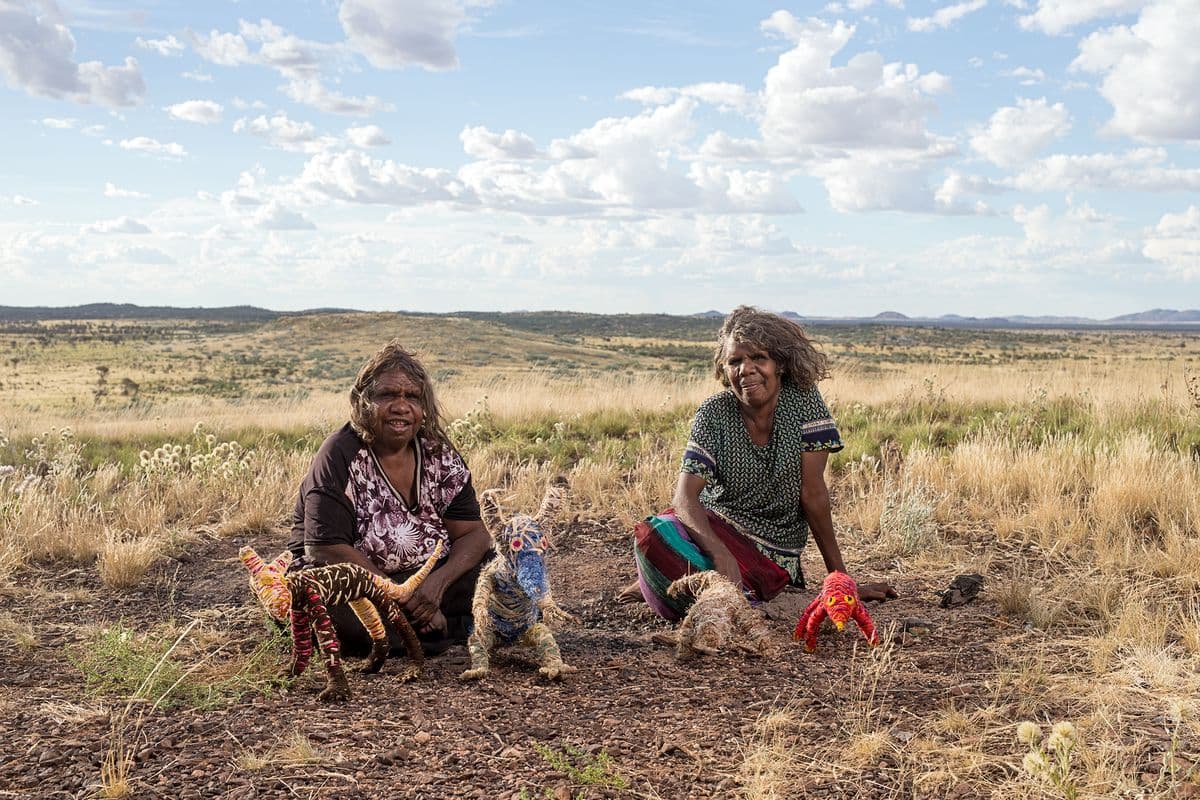 Two Indigenous Australian woman are on Country sitting with their sculptures of small animals woven from native and dyed grasses