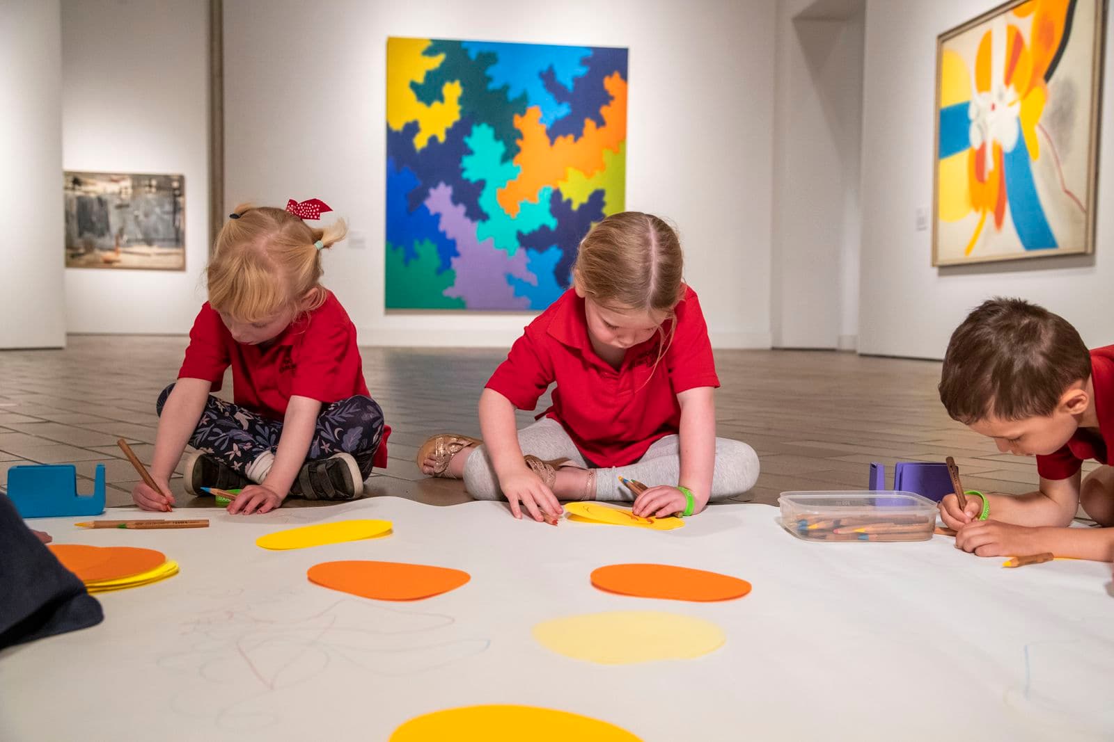 A group of primary school children sit on the gallery floor and work together on an artwork