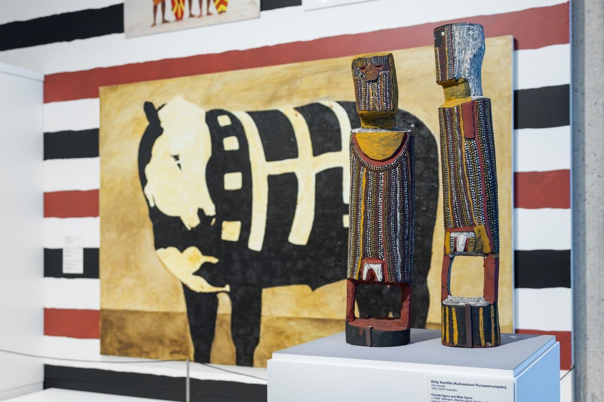 Two tiwi sculptures in front of a painting of a cow