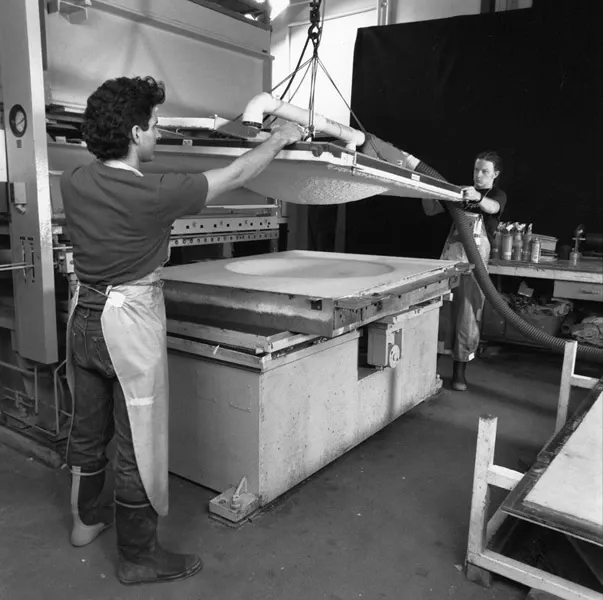 Black and white photo of two men lowering paper pulp dome onto press bed