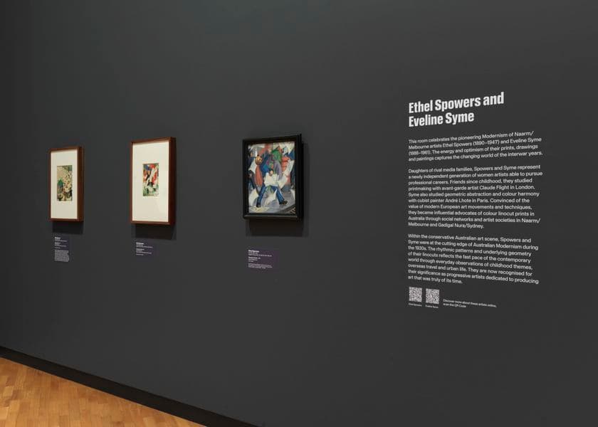 A grey wall with an exhibition didactic panel on the right and three works on art on the left