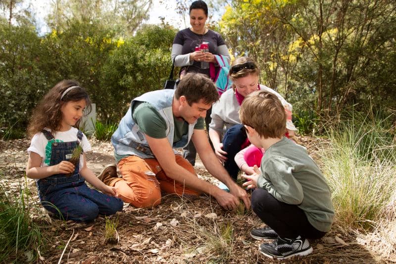 Photograph of a family group crouching in the garden beds of the Sculpture Garden