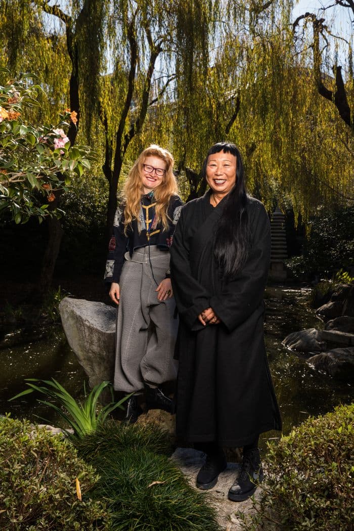 Two women are smiling and standing next to each other posing for a photo in a lush green garden