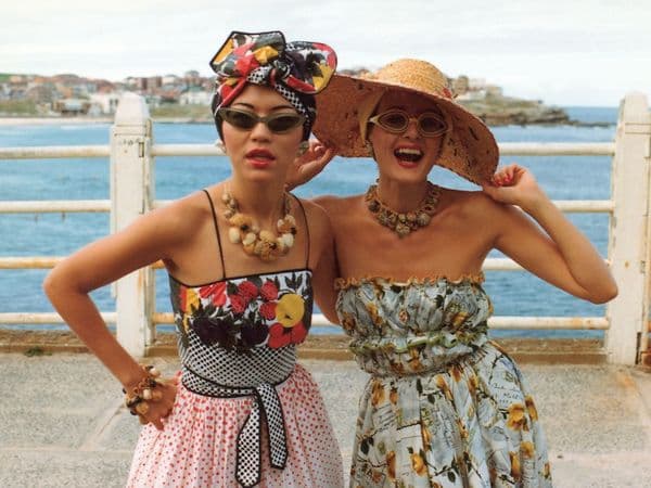 Two women wearing glamorous clothes, hats and jewellery pose together