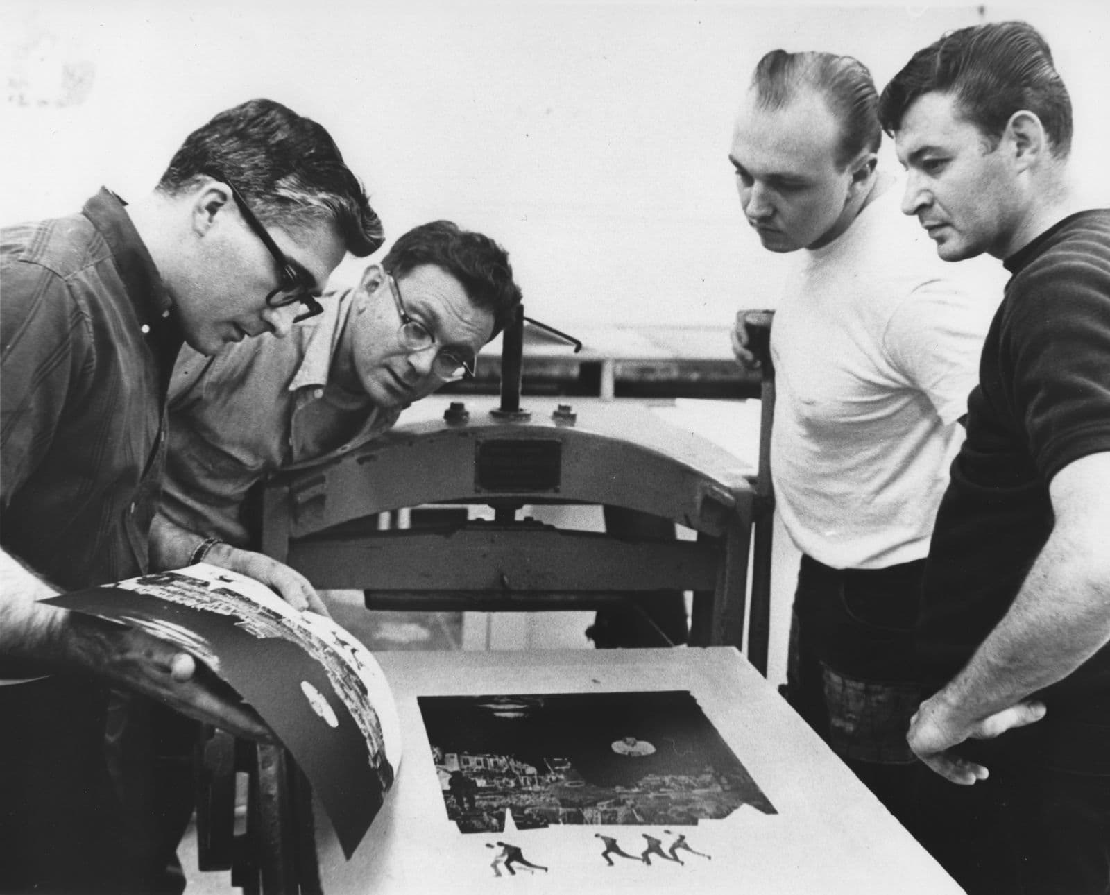 Four men looking at paper with freshly printed artwork on it